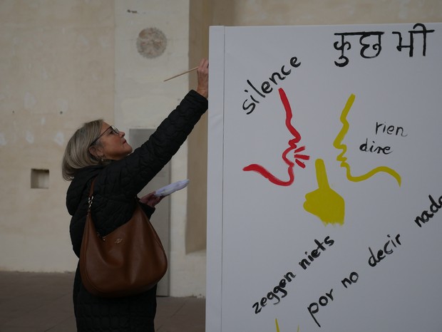 Eine Frau malt auf eine Leinwand. Darauf sind Schweigesymbole und unterschiedliche Sprachen gemalt. Eine Frau malt auf eine Leinwand. Darauf sind Schweigesymbole und unterschiedliche Sprachen gemalt.