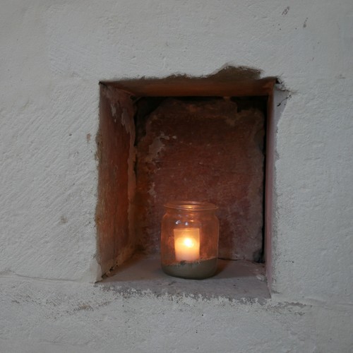 In einer kleinen Wandnische steht eine Kerze in einem Glas.