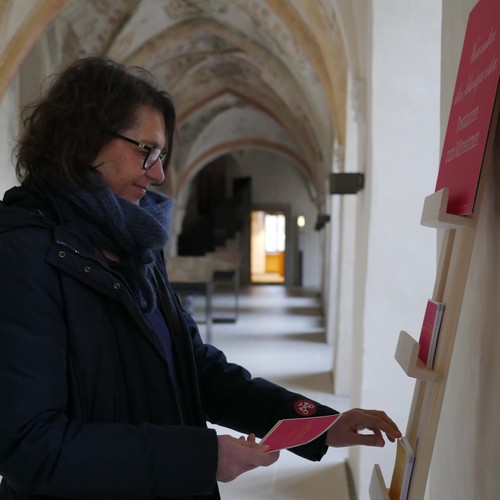 Eine Frau steht an einem Postkartenständer im Kreuzgang des Klosters Dalheim.