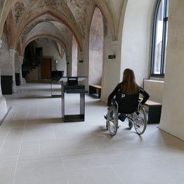 Eine Frau fährt im Rollstuhl durch den Kreuzgang und sieht sich um.