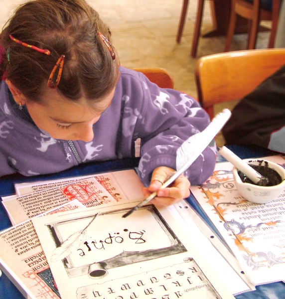 Ein Mädchen schreibt mit einer Gänsefeder. Auf dem Tisch steht ein Mörser mit Tinte.