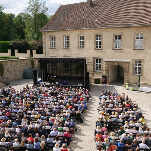 Im Ehrenhof sitzen viele Menschen auf Stühlen und schauen zur Bühne.