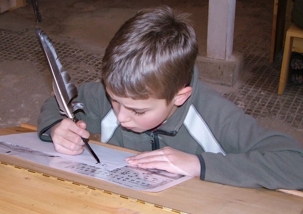 Ein Junge schreibt mit einer Feder.