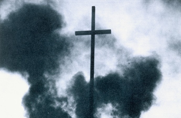 Ein von Rauch umgebenes Kreuz. Das Foto ist schwarz-weiß.