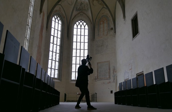 Eine Person mit Kamera filmt in der Dalheimer Klosterkirche. Rechts und links stehen schwarze Stuhlreihen.