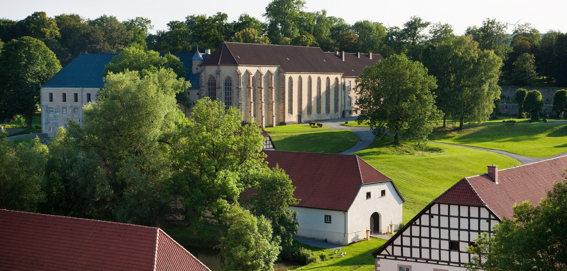 Blick auf die Klosteranlage mit Kirche, Scheunen und Wiesen.