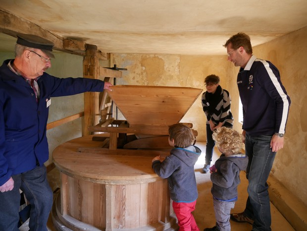 Der Müller zeigt einer Familie in der Mühle, wo das Schrot gemahlen wird.