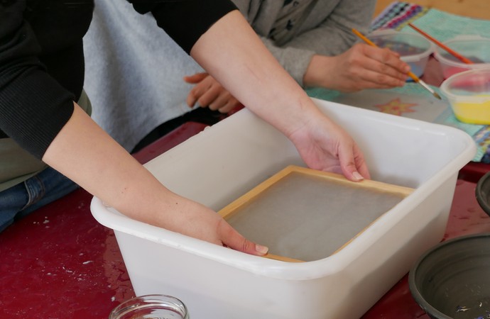Hände schöpfen Papier in einer Wanne