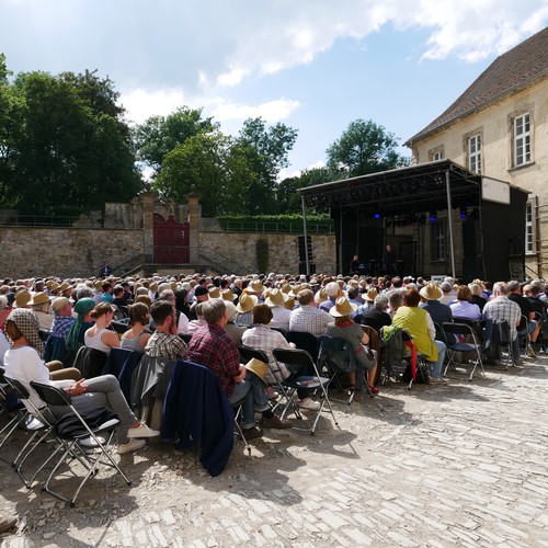 Im Ehrenhof sitzen viele Menschen auf Stühlen und schauen zur Bühne.