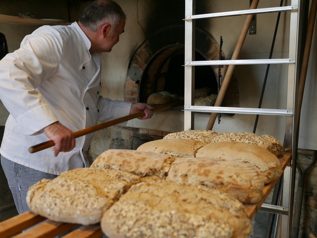 Ein Bäcker holt fertig gebackene Brote aus dem historischen Backofen.