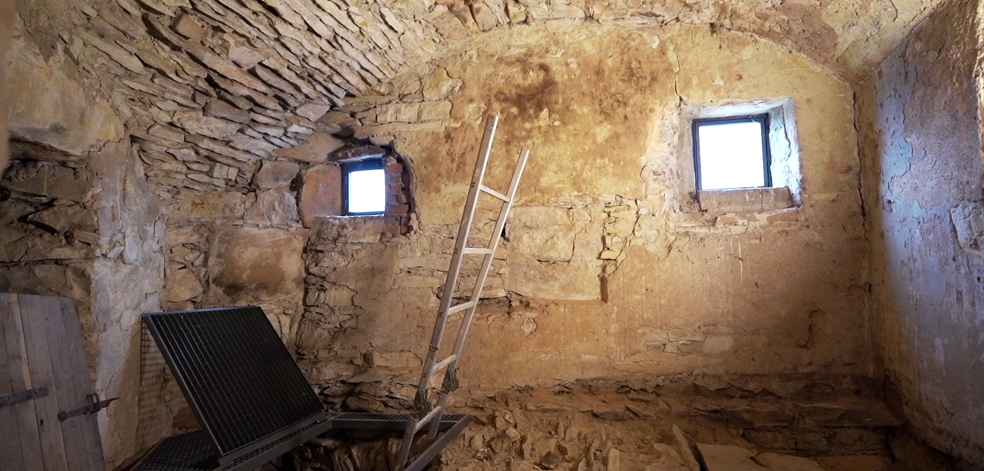 Ein kleiner Raum mit Steinfußboden und -decke, in dem eine Leiter nach unten führt.