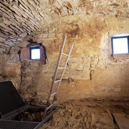 Ein kleiner Raum mit Steinfußboden und -decke, in dem eine Leiter nach unten führt.