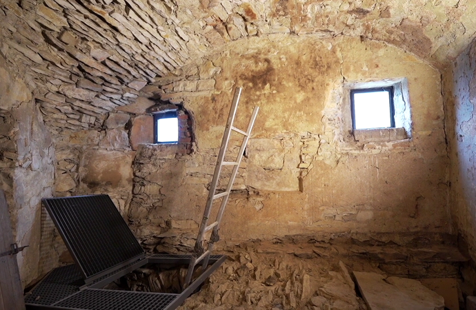 Ein kleiner Raum mit Steinfußboden und -decke, in dem eine Leiter nach unten führt.
