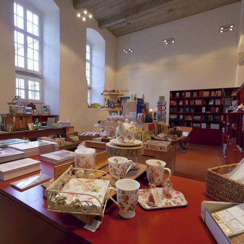 Museumsshop mit Tischen und einem Kartenständer und einem Teeservice und Büchern im Vordergrund.