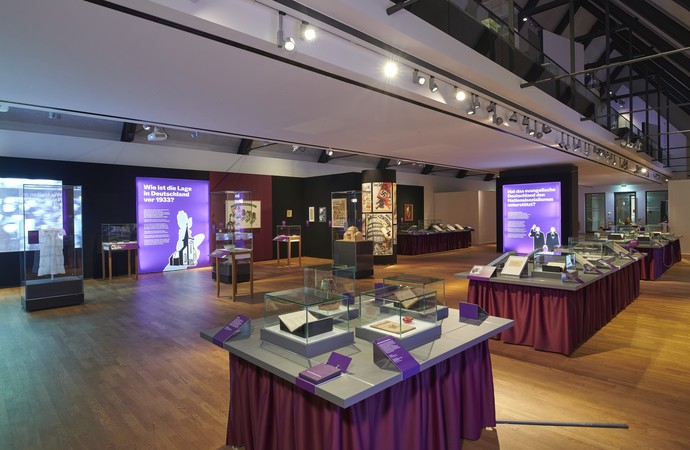 Blick in die Sonderausstellung. Ein Tisch im Vordergrund. Vitrinen und illuminierte Tafeln im Hintergrund