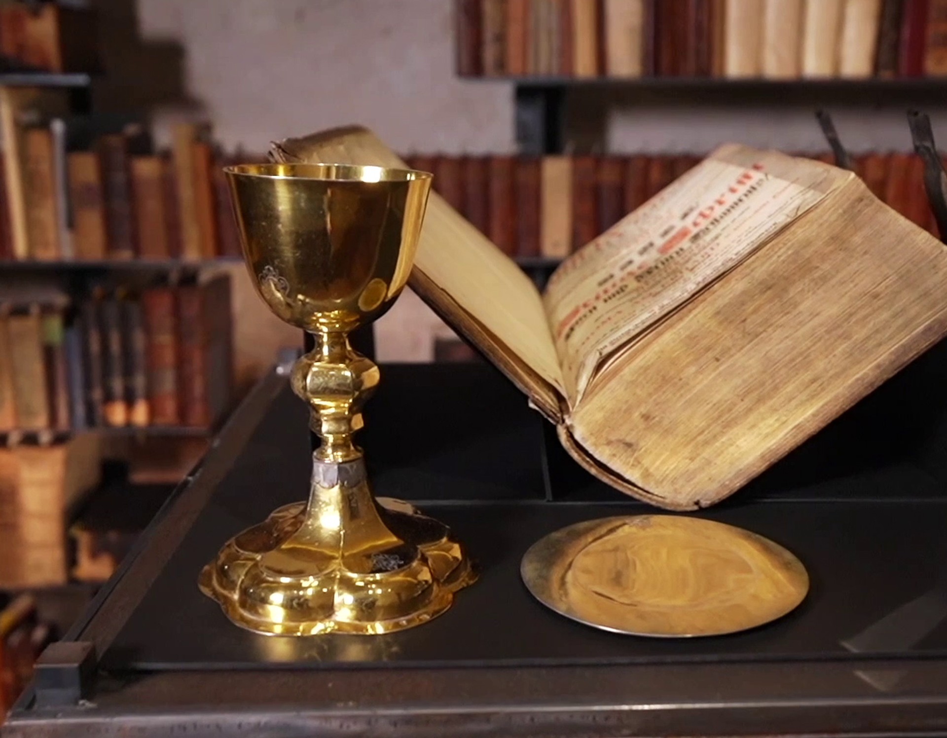 Ein goldener Kelch steht neben einer sehr alten, aufgeschlagenen Bibel. Beide sind Exponate aus dem Kloster Dalheim.