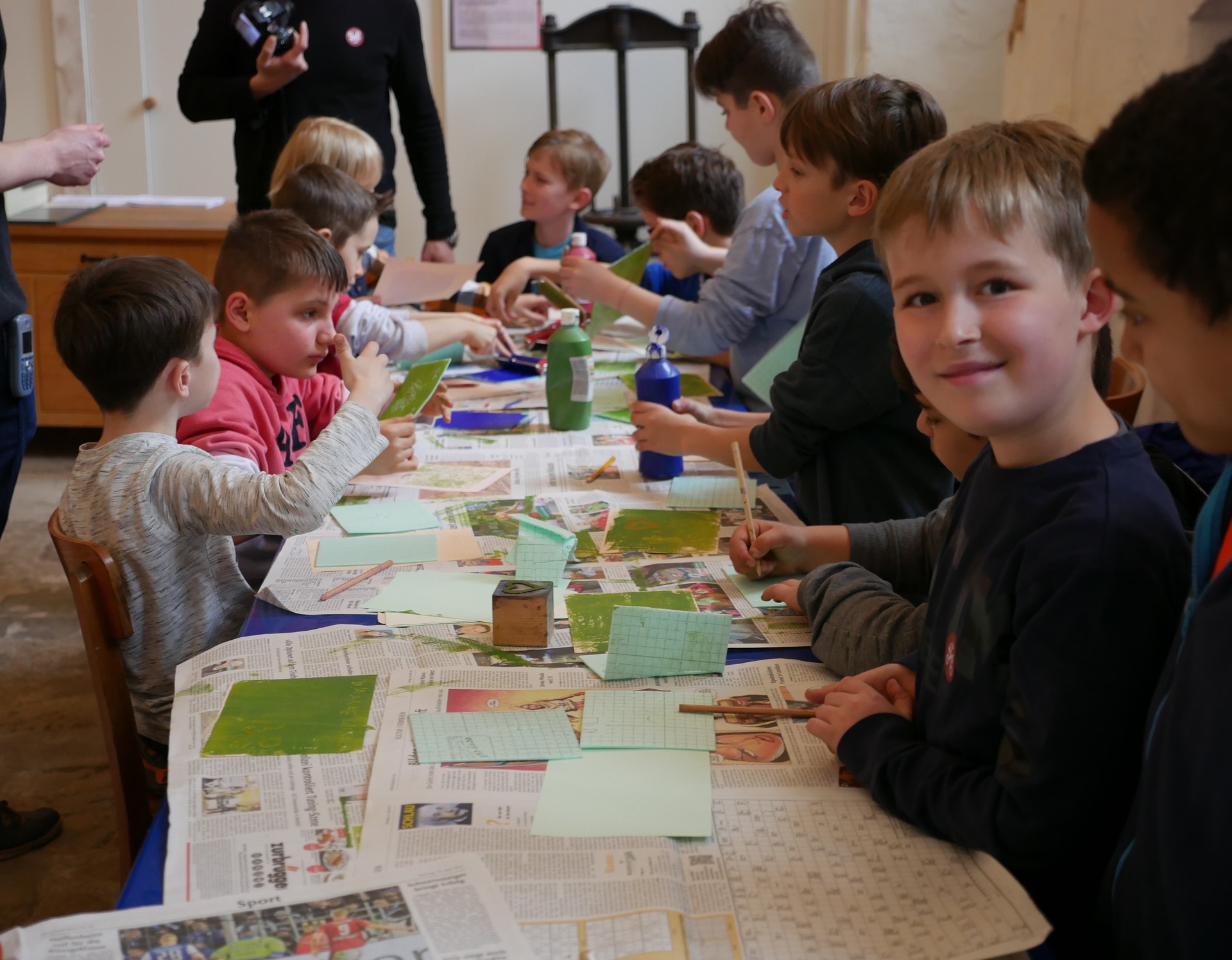 Viele Kinder sitzen an einem Tisch und bedrucken Karten mit Stempeln.