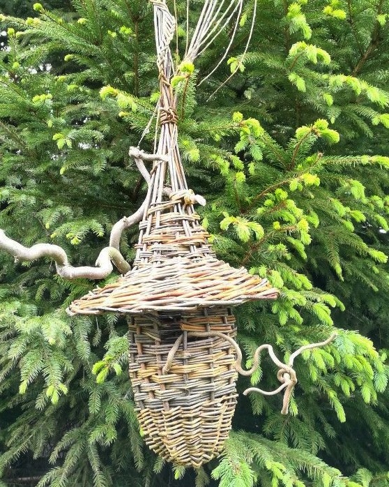 Ein aus Weiden geflochtenes Vogelhäuschen hängt im Baum.