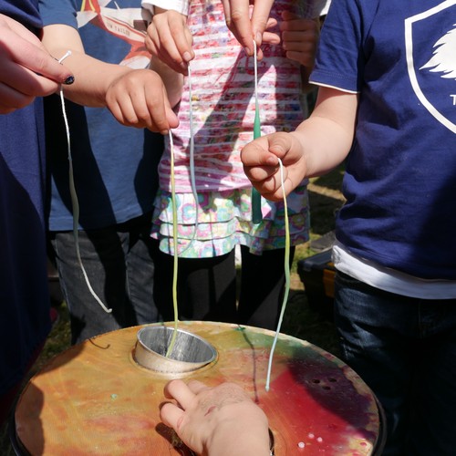 Auf dem Bild sind viele Kinderhände zu sehen, die einen Kerzendocht über einem Wachsbottich halten.