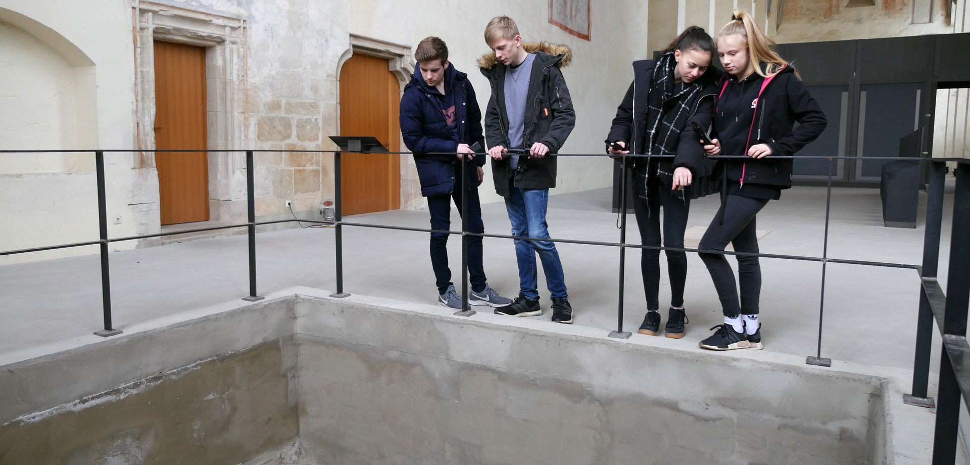 In einer Kirche stehen vier Jugendliche an einem Geländer und schauen in die davor liegende Grube.