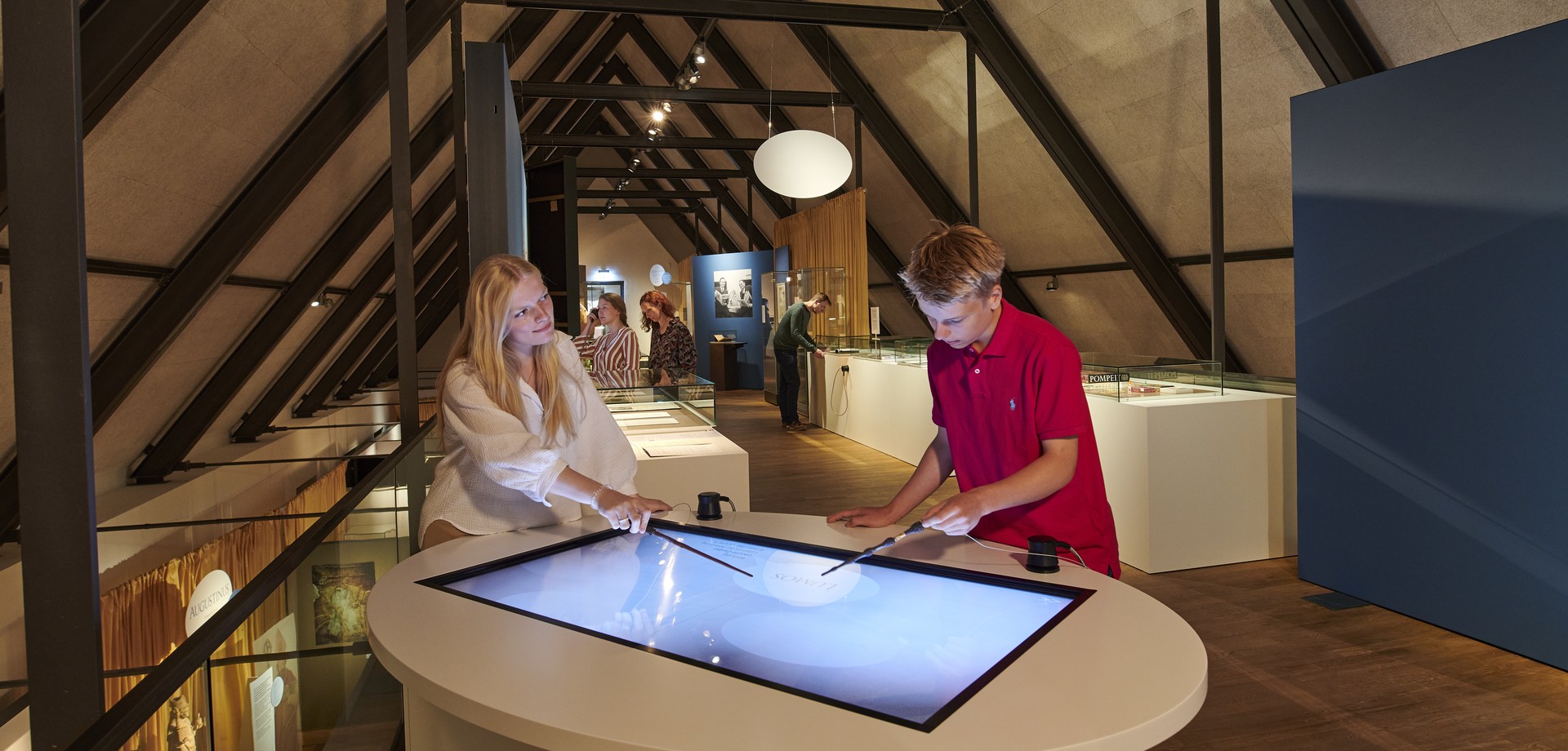 Ein Jugendlicher und eine junge Frau nutzen die interaktiven Medienstationen in der Sonderausstellung "Latein. Tot oder lebendig".