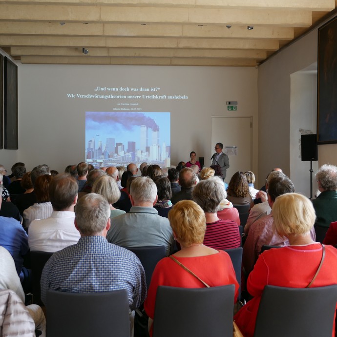 Vortragsveranstaltung im Vortragsraum mit Publikum und einer Präsentation an der Wand. (vergrößerte Bildansicht wird geöffnet)