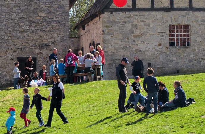 Familien sitzen auf Bänken oder der Wiese vor dem ehemaligen Hühnerhaus.