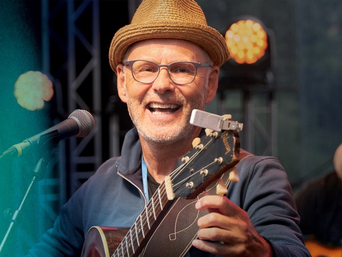 Reinhold Beckmann spielt Gitarre. Er schaut sehr freundlich.