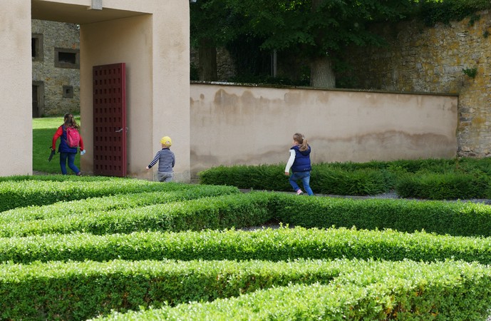 Drei Kinder rennen durch ein rotes Tor im Klostergarten.