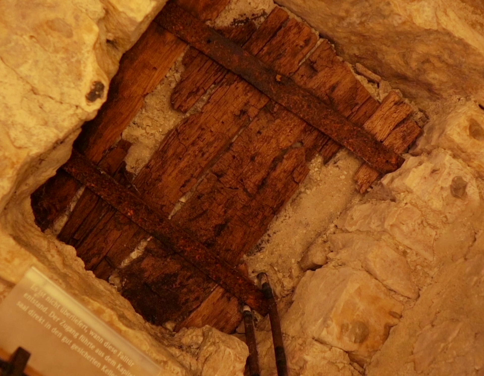 Die Überreste einer alten Falltür aus Holz sind in der Decke des Kellers zu sehen.