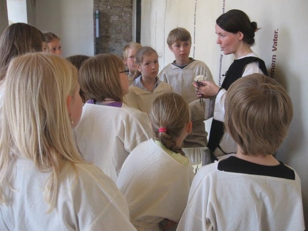 Eine Gruppe von Kindern in weißen Hemden steht um eine Frau, die gerade spricht.