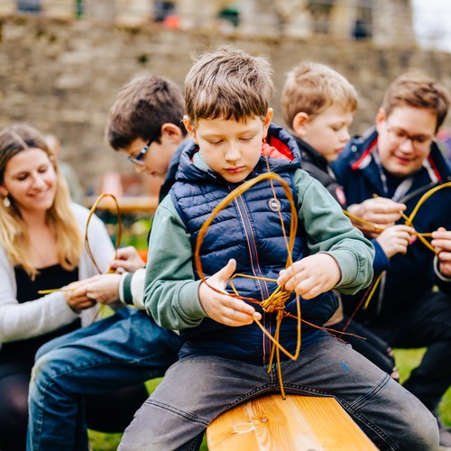 Ein Junge auf einer Bank beim Korbflechten.
