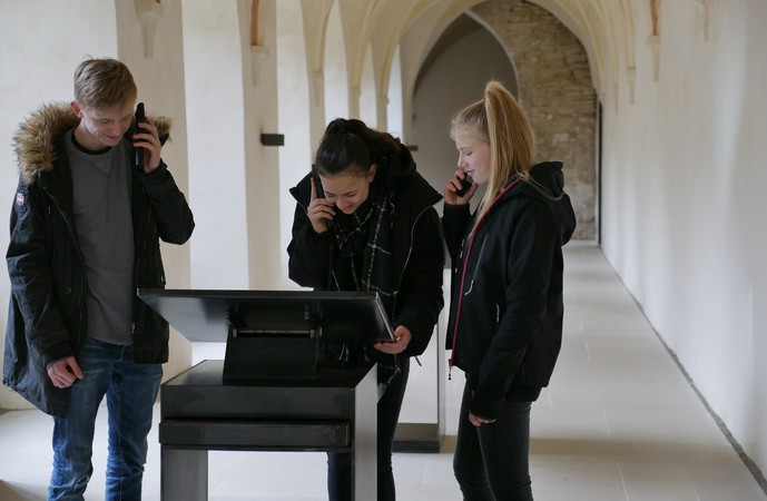 Drei Jugendliche hören sich den Audioguide in der Klausur an.